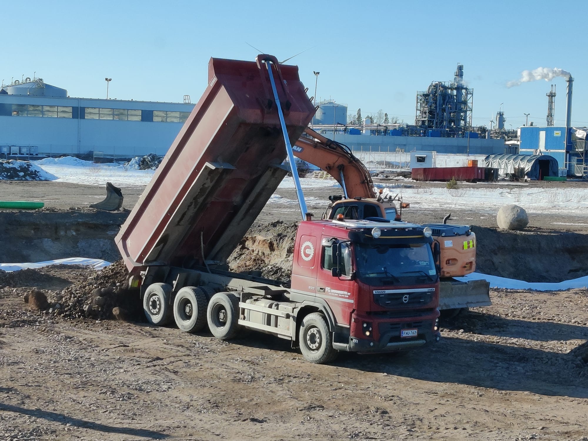 Punainen Volvo FMX maansiirtoauto kippaamassa massoja työmaalla